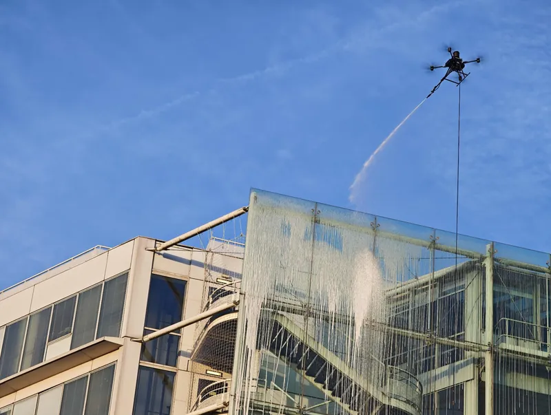 Tethered drone sending a water jet onto the glass stair tower of Hôpital européen Georges-Pompidou