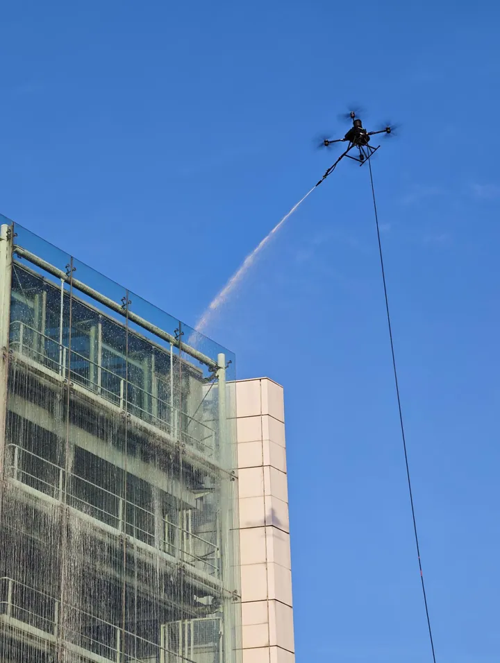 Water jet from the tethered drone reaching the upper glass panels of the stair tower