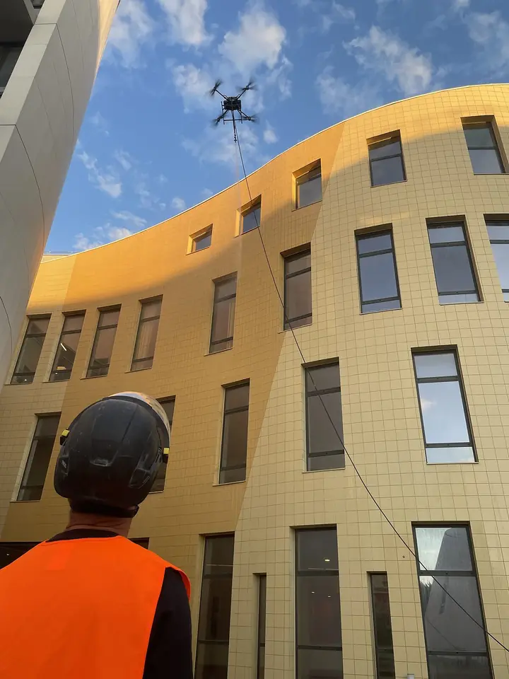 Pilot and drone along a curved yellow façade