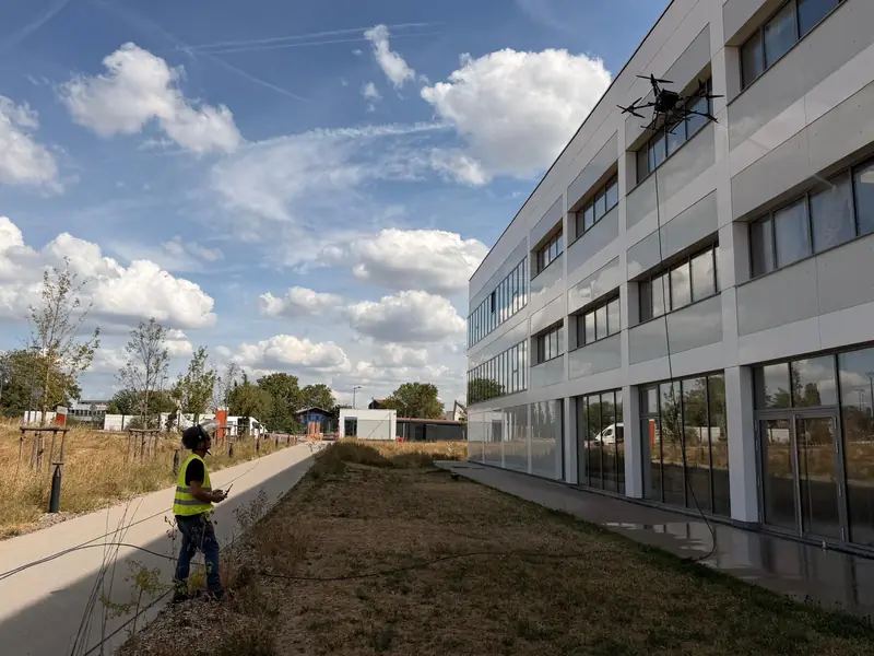 CleanAlta pilot on the ground flying the tethered drone along a glass façade